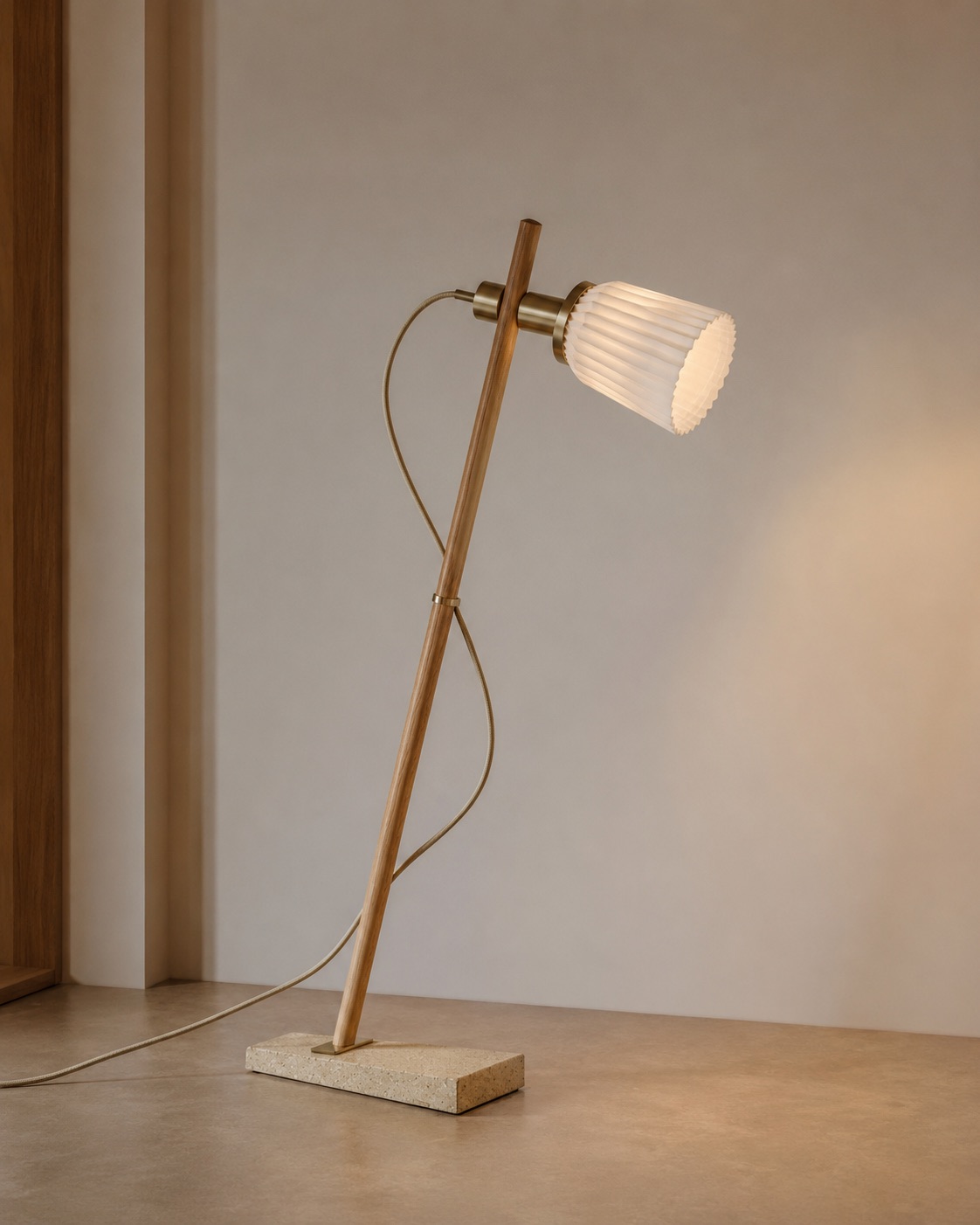 Angled wood and brass table lamp with a pleated cone shade on a terrazzo base