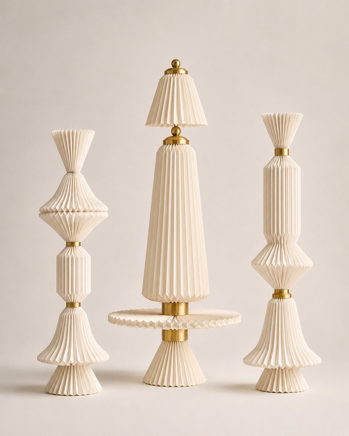 Three tall pleated paper totem sculptures with brass rings